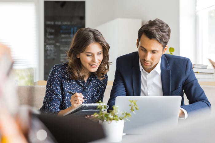 A man and woman sit at a cafe and work on a laptop.