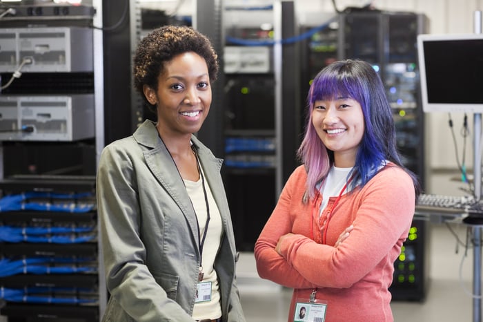 Two employees stand in front of rows of computer servers.