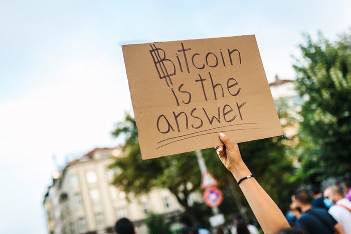 A person holding a cardboard sign up that reads, Bitcoin is the answer. 