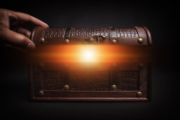 A hand starts to open a miniature treasure chest, revealing a glowing interior. 