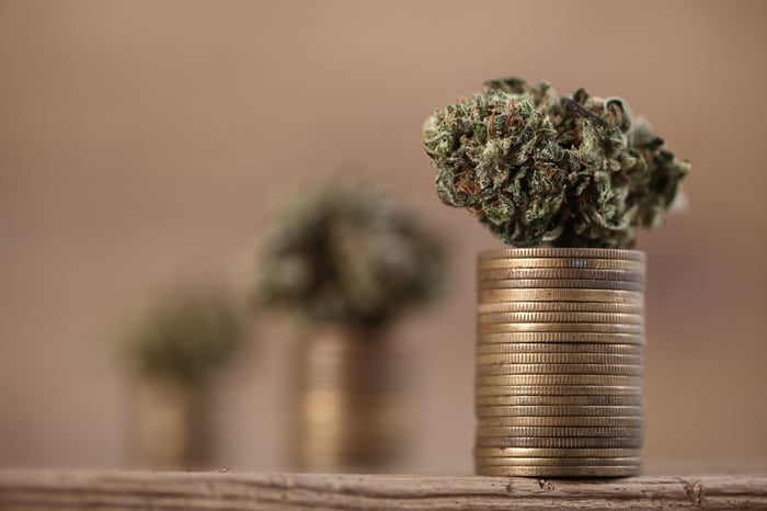 A marijuana bud on top of rising stacks of gold coins.