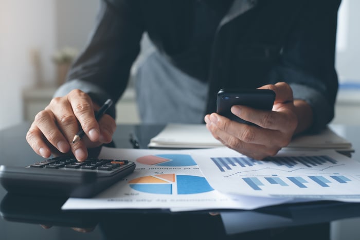 Holding a smartphone, a man works with financial charts and a calculator.