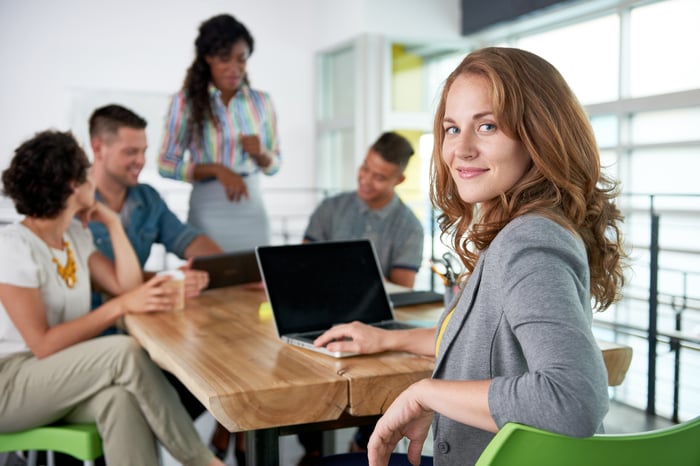 Smiling businesswoman looking at camera with coworkers in the background