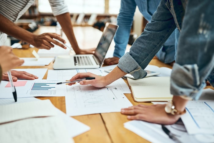 People working at a table with multiple charts scattered on it.