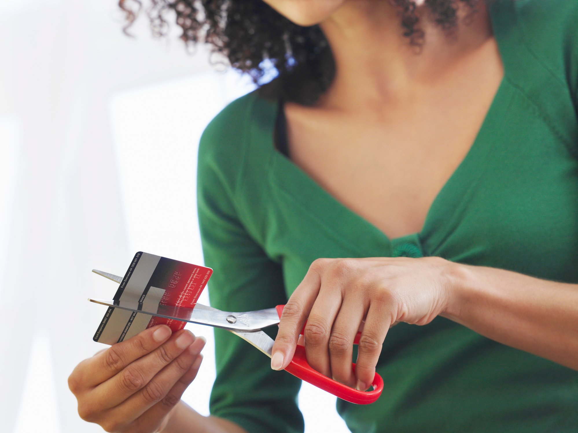 young woman cutting credit card in half with scissors debt POC