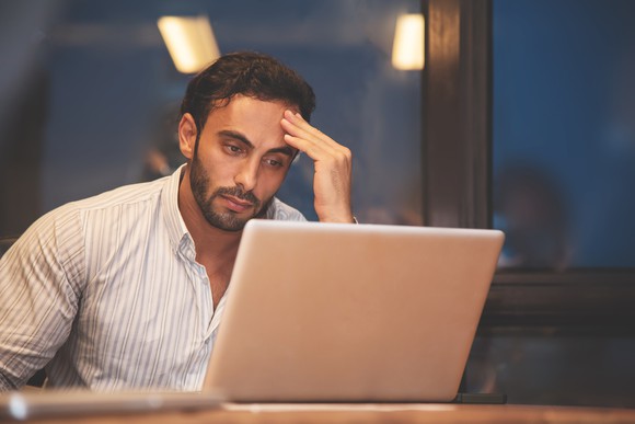 Man holding his head while looking at laptop