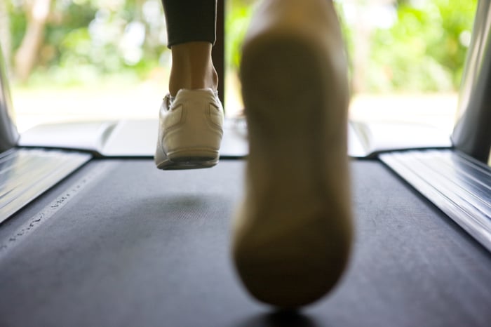 Close-up of the ankles and shoes of a person running on a treadmill.