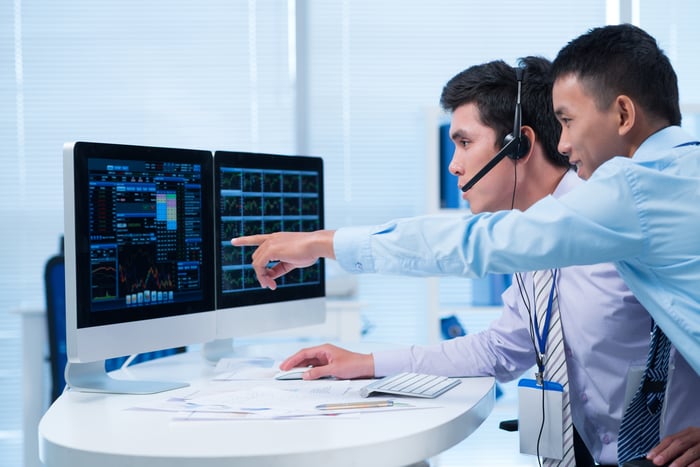 Happy broker showing some stocks to his colleague on computer screen.