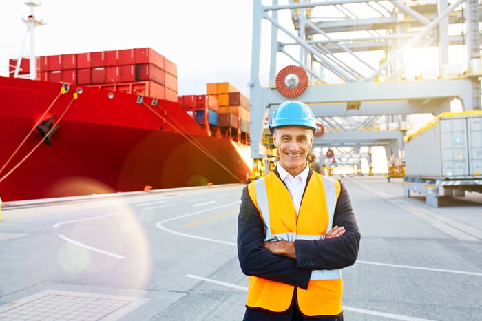 Smiling man in a hard hat in front of a loaded container ship