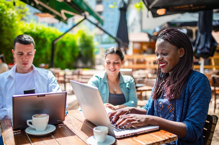 Three people at a table using laptops and drinking coffee.