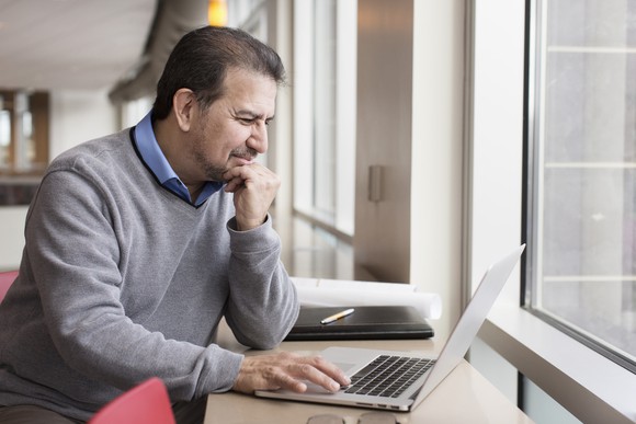Man squinting while resting hand on laptop