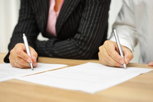 Two people sitting down and signing a document each.