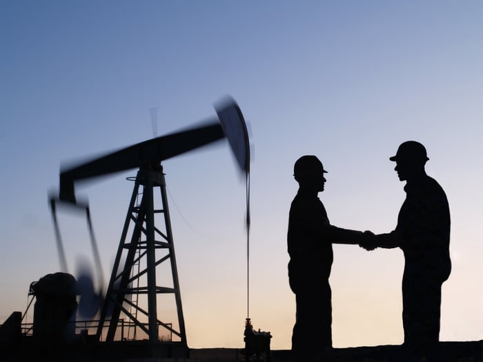 The silhouette of two people shaking hands near an oil pump.