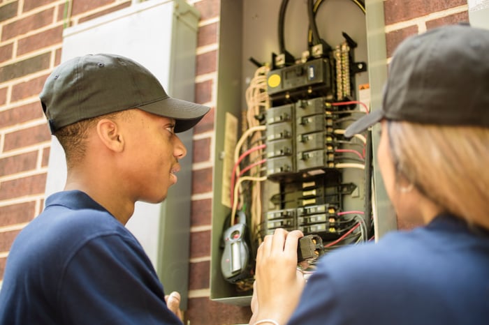 Two people working with a electric power box.