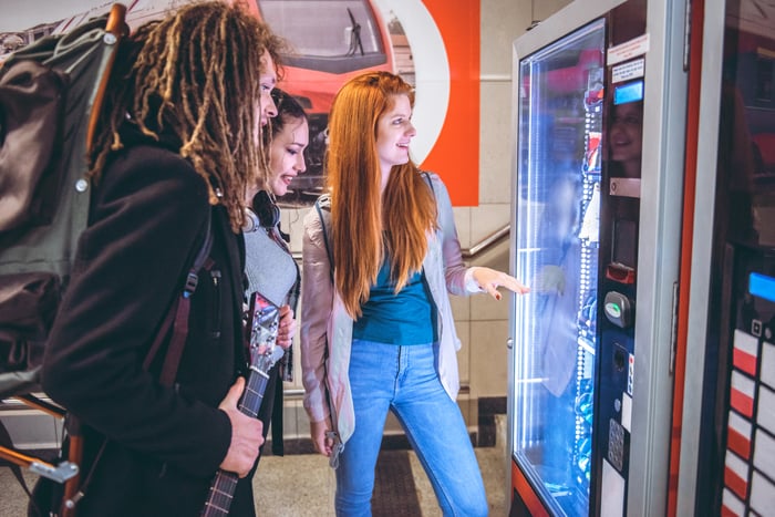 Friends checking out products in a vending machine while smiling