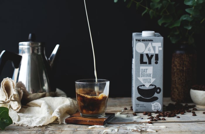 A box of Oatly next to coffee.