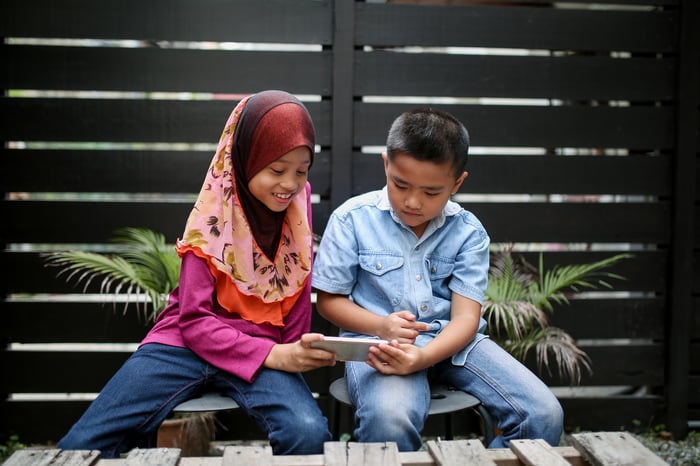 Two kids are playing on a phone. 