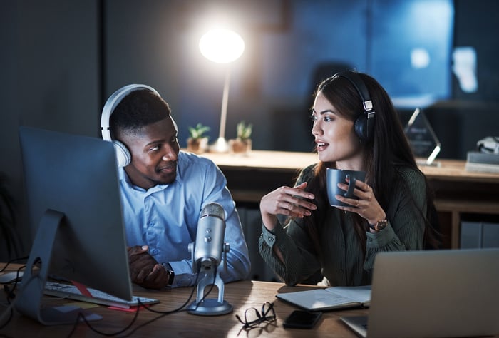 Two people doing a broadcast while sitting in an office at night. 