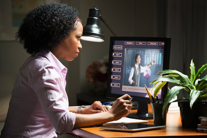 A woman sits at her computer watching an instructor online.