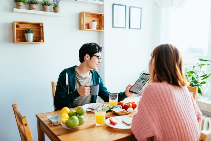 Two people sit at the breakfast table and look at a tablet.