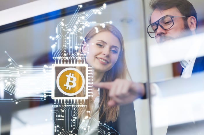 Two people looking at a digital Bitcoin logo.