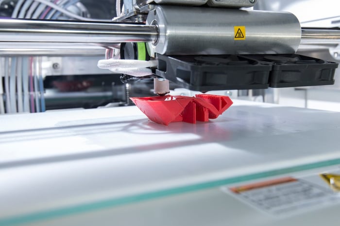 Close-up of an industrial 3D printer producing a red plastic object.