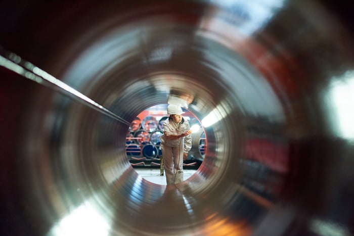 A person in a hard hat looking through an empty pipeline.