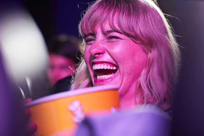 A person laughing in a movie theater with a large popcorn bucket.