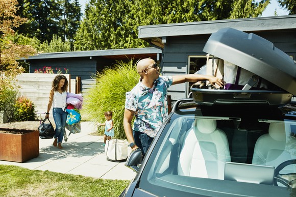 A family loads luggage into a car top carrier in preparation to travel.