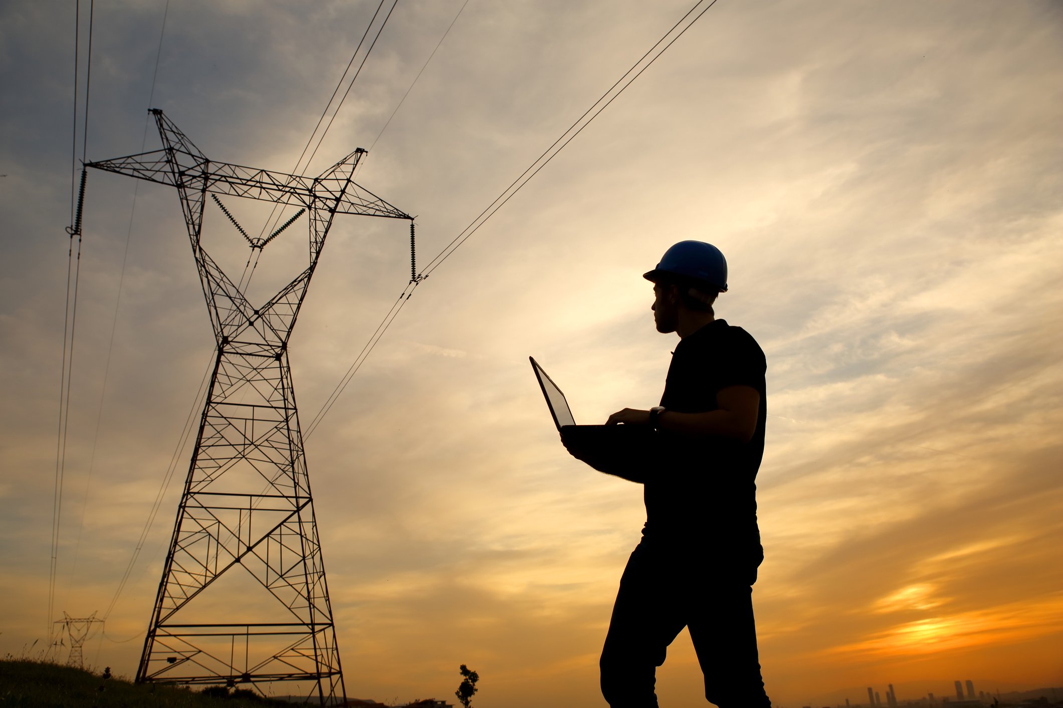 Worker with a laptop examines an electric tower and power lines