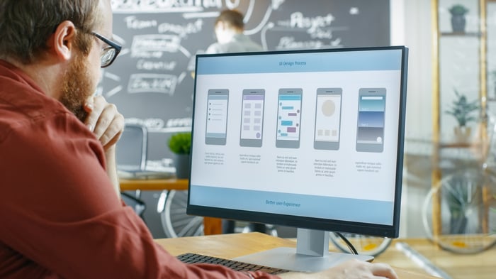 A man looking at a computer monitor and  working on app development.