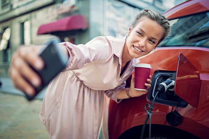 Young lady taking selfie with electric vehicle showing power cord plugged in