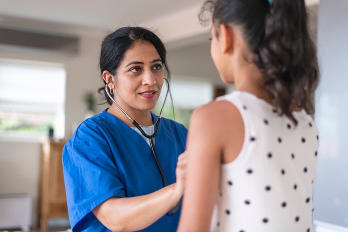 A pediatrician using a stethoscope to listen to the heart and lungs of a child.