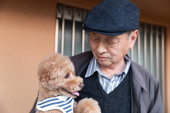 An elderly man holding a happy poodle. 