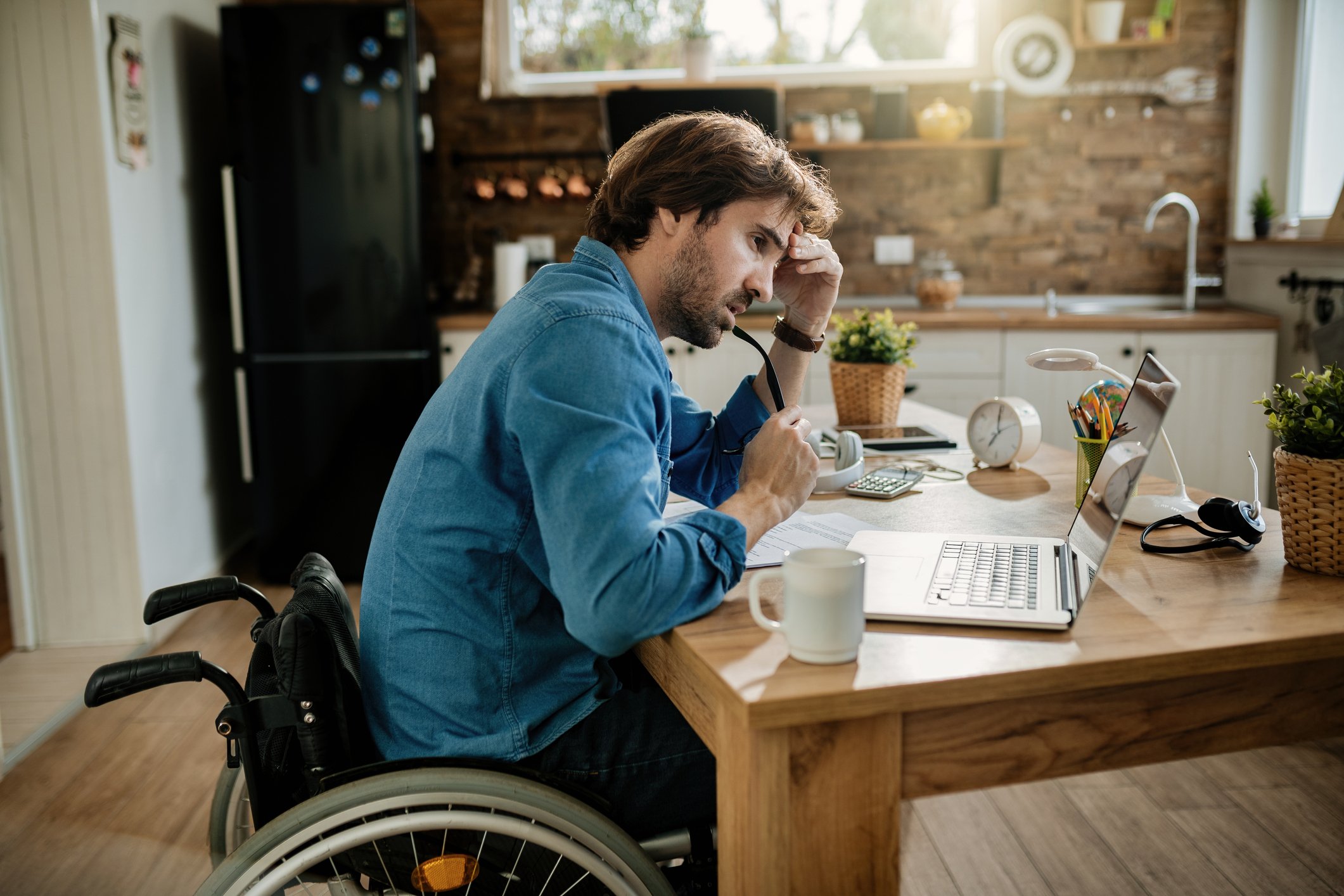 Appearing concerned a man who uses a wheelchair looks at a laptop.