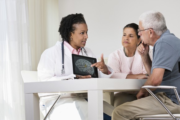 A doctor shows a brain scan to an older couple looking on intently.
