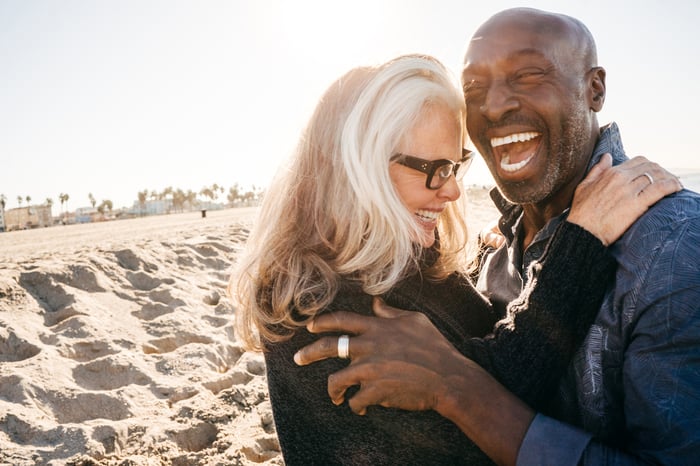 Retired couple hugging and laughing on the beach.