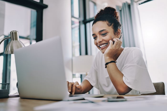 Smiling young person with hand on chin looking at laptop.