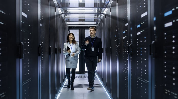 Two IT technicians walking in a data center between rows of rack servers.