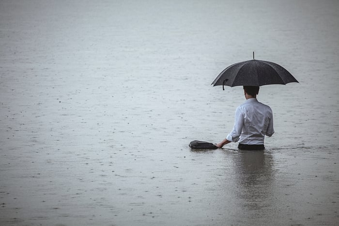 Man wading into water while holding an umbrella in the rain.