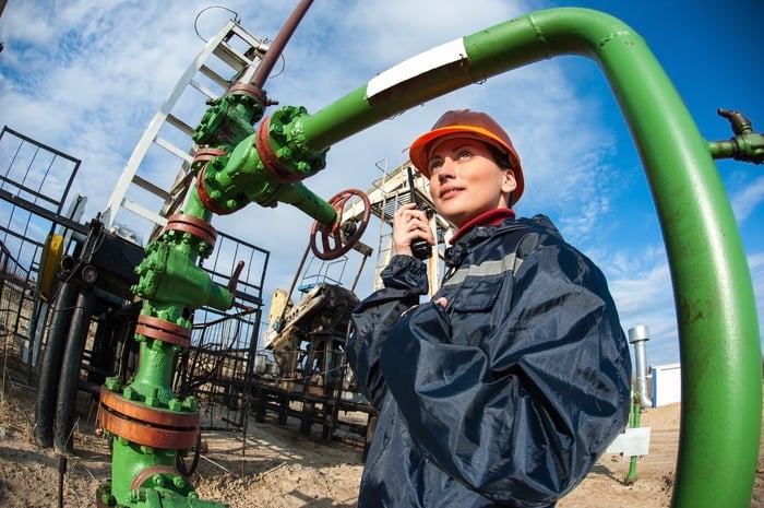 An oil and gas engineer speaking on a two-way radio while standing under pipeline. 