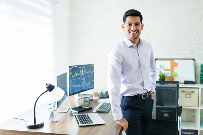 Person leaning on desk with computer monitor showing graphs on screen