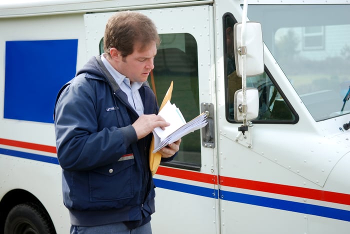 Mailman leafing through mail next to a postal-delivery truck.