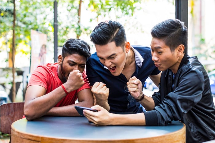 Three people celebrate victory in a mobile smartphone game.