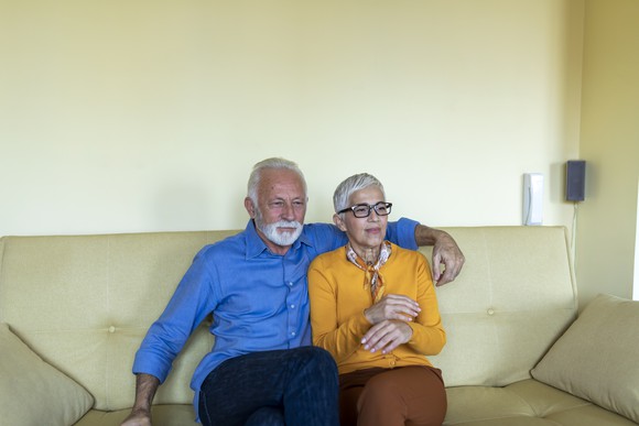 Two older people sitting together on a couch watching something.