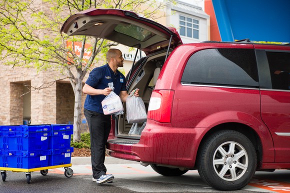 A man in a Walmart vest loading groceries into the trunk of a minivan.