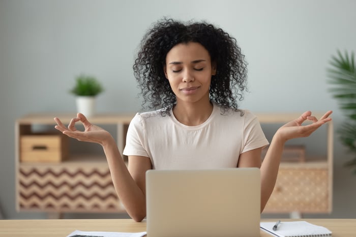 Relaxed person meditating at a desk in front of a laptop.