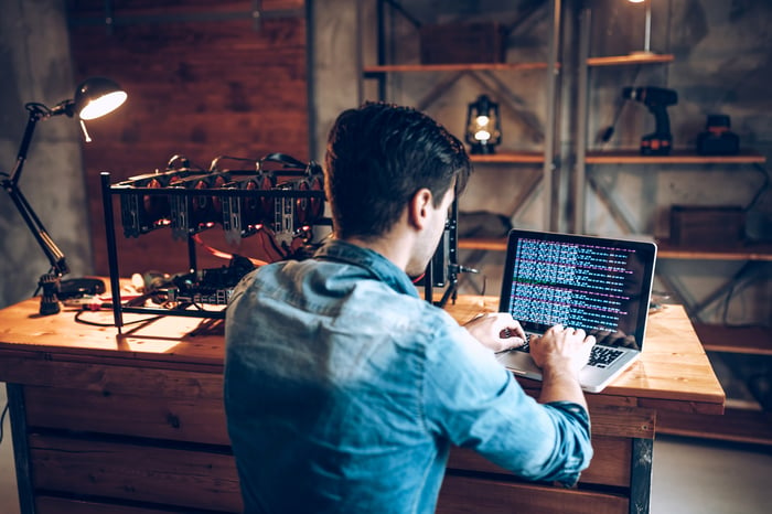 A person programs code into a computer with cryptocurrency mining equipment attached.