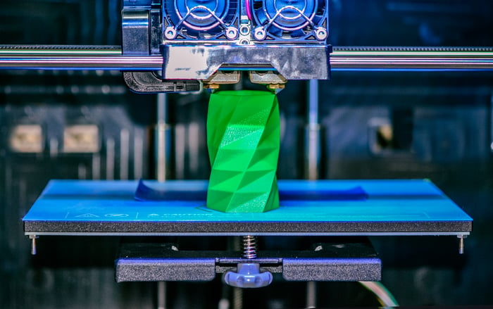 Close-up of a 3D printer producing a green plastic object.