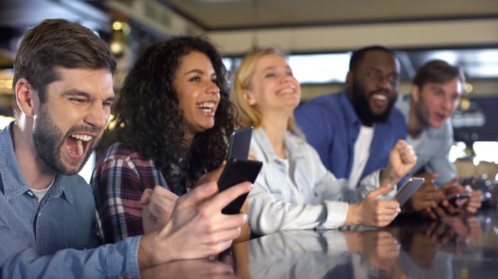 Sports fans betting online by smartphone app sit together at a bar.